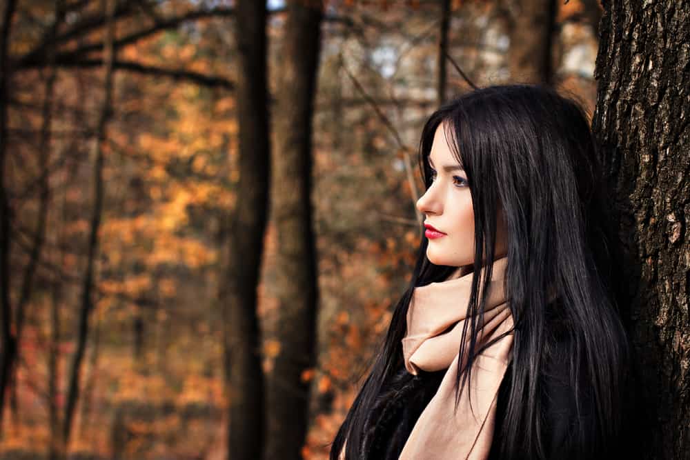 une femme aux longs cheveux noirs appuyée contre un arbre