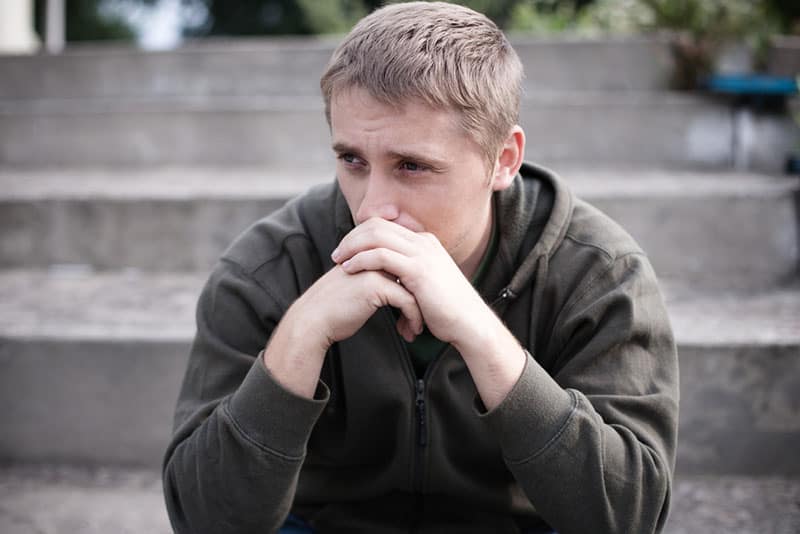 homme blond triste assis à l'extérieur