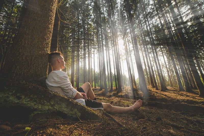 jeune homme assis sur le sol dans la forêt