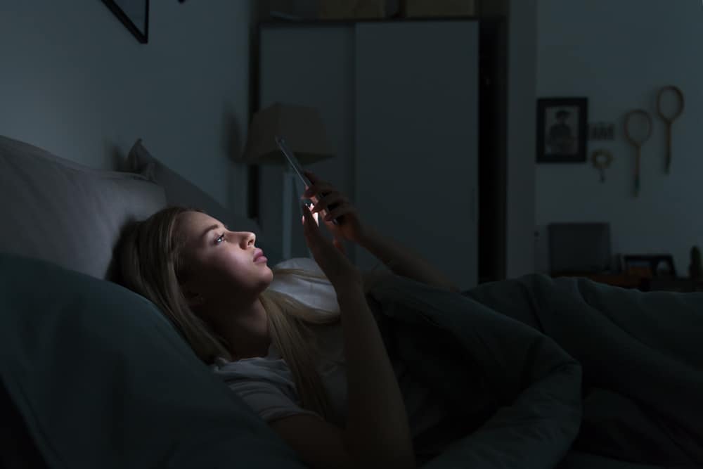 la femme est allongée dans son lit avec le téléphone à la main