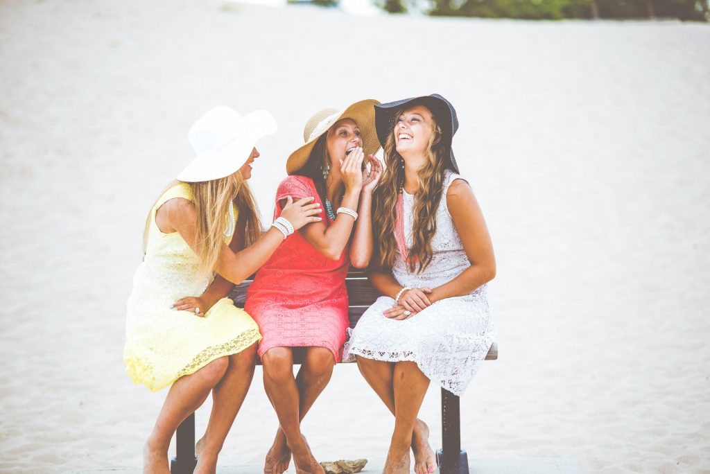 trois femmes sont assises sur un banc avec des chapeaux sur la tête et rient