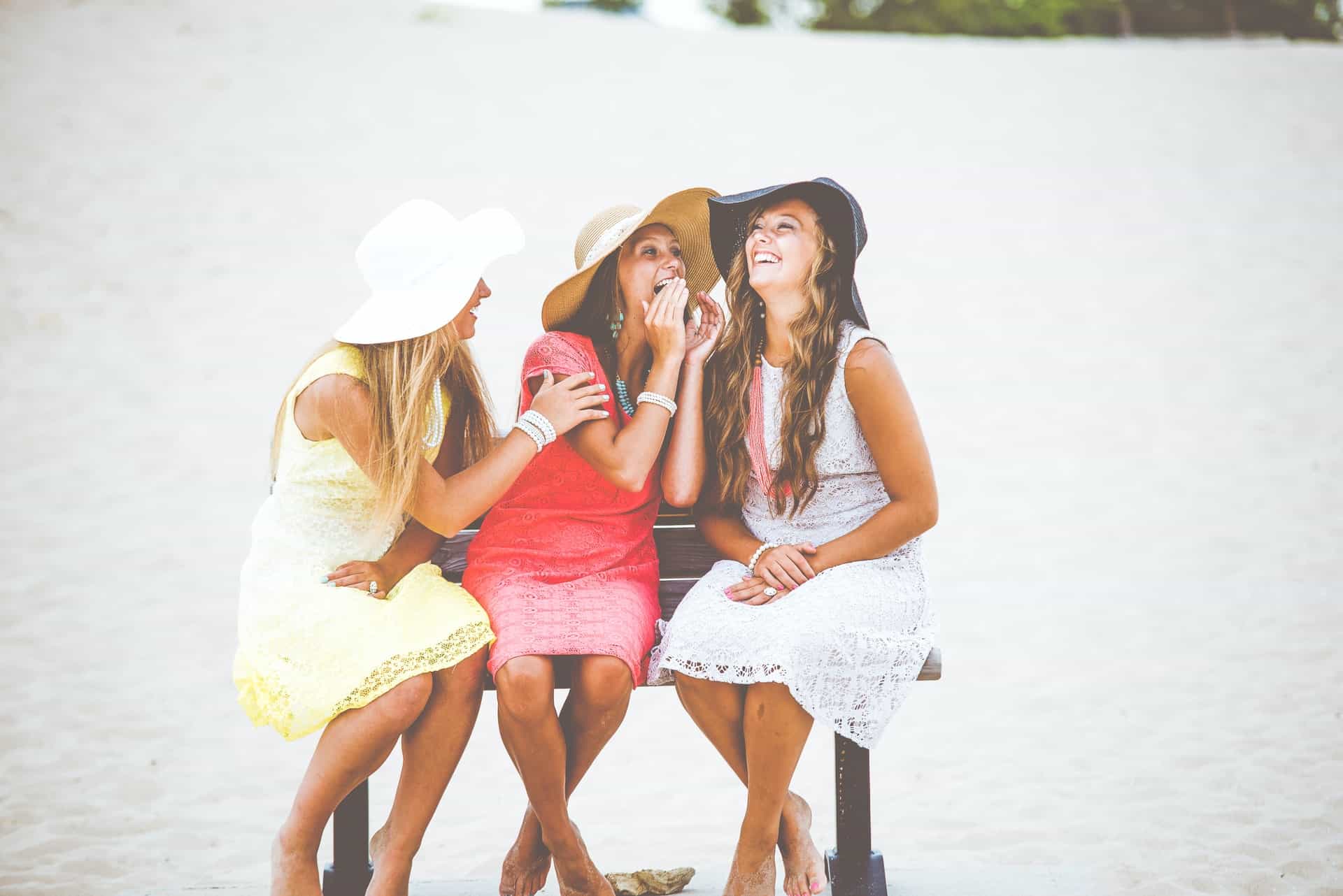 tres mujeres están sentadas en un banco con sombreros en la cabeza y riendo