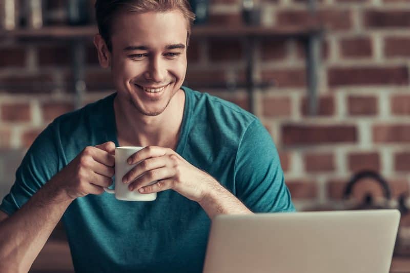 un homme est assis devant un ordinateur portable et boit du café
