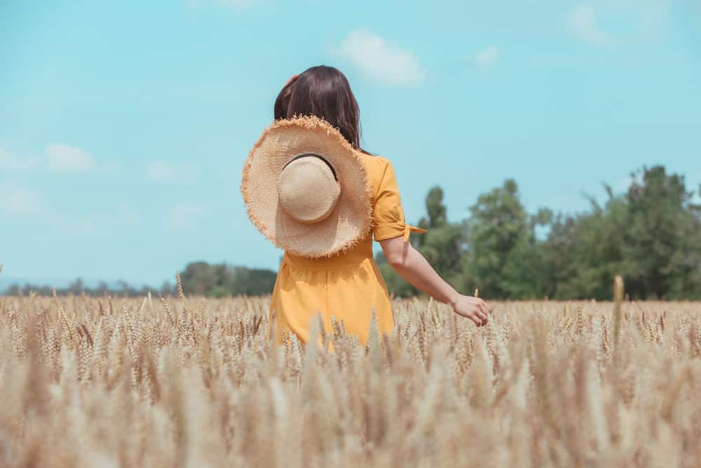 une femme en robe jaune définit un champ de blé