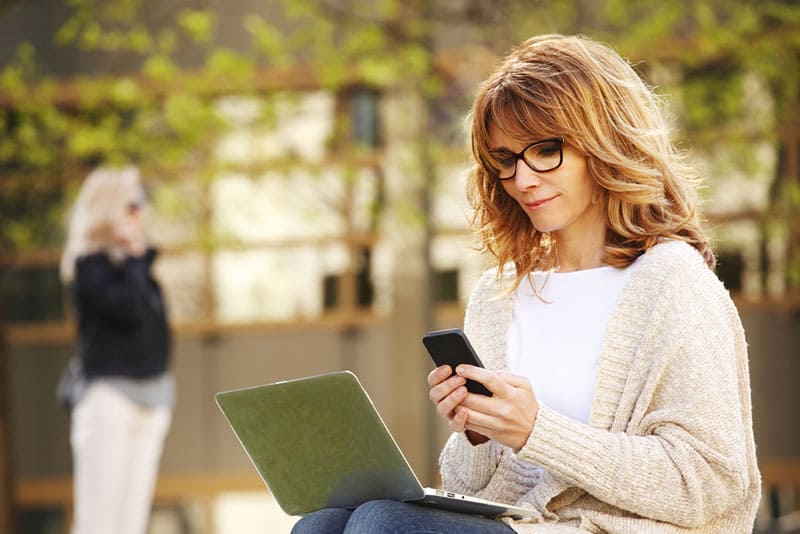 femme blonde avec ordinateur portable sur ses genoux et téléphone à la main