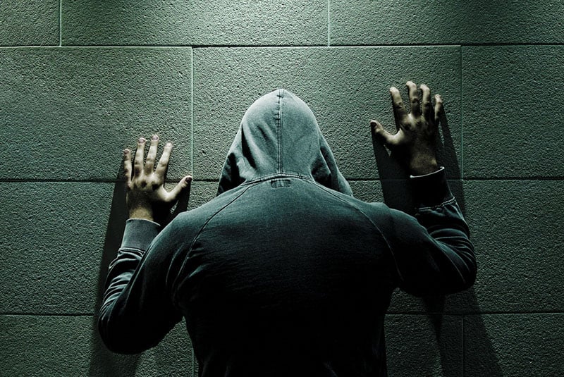 homme dans un sweat à capuche avec les mains contre le mur