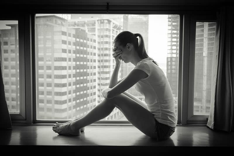 photo noir et blanc d'une jeune femme triste près de la fenêtre
