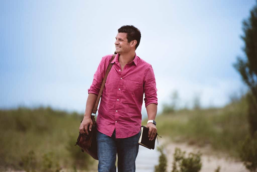 un homme pose avec un sac et un livre à la main