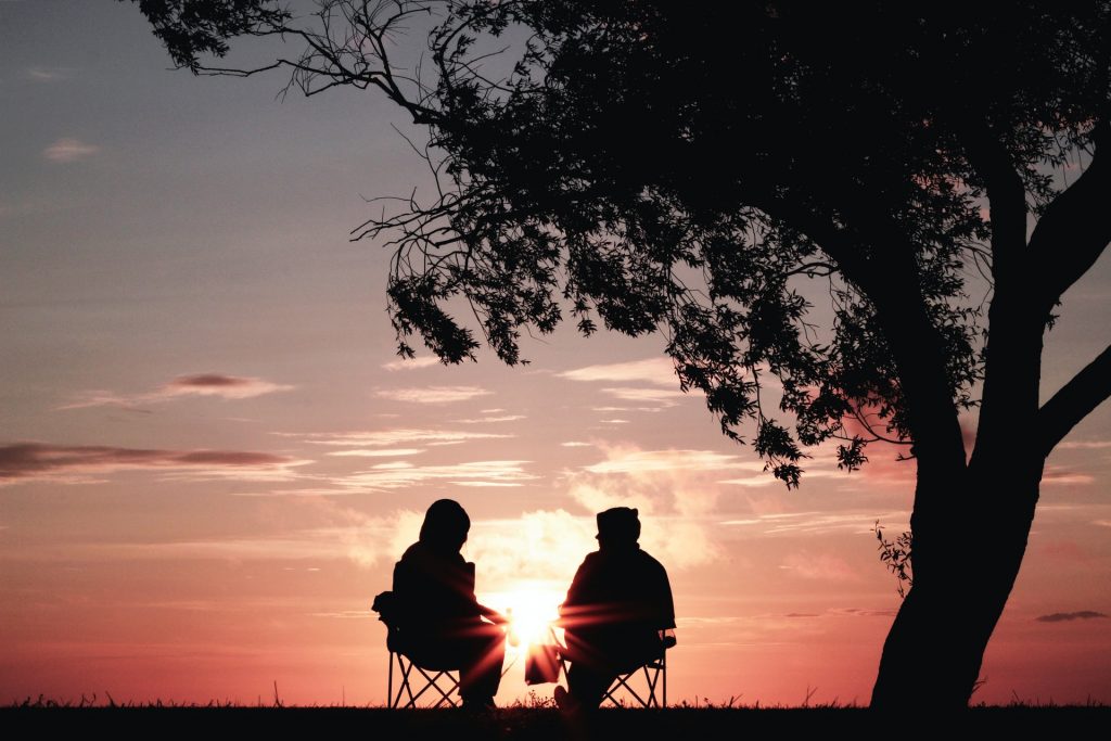 un homme et une femme parlent à une table au coucher du soleil