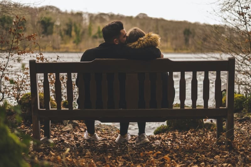un homme et une femme sont assis sur un banc, il l'embrasse sur le front