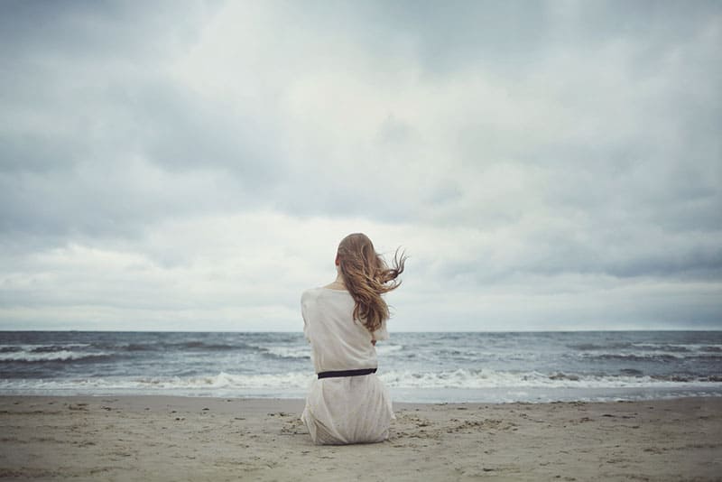 jeune femme blonde solitaire sur la plage assis
