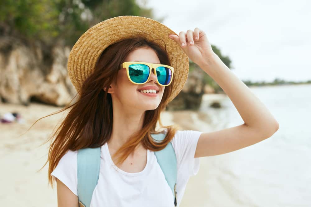 la femme marche sur la plage avec des lunettes et un chapeau sur la tête