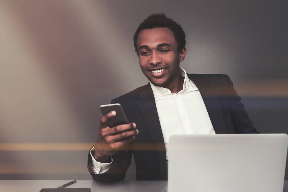un homme est assis derrière un ordinateur portable et tient un téléphone dans sa main