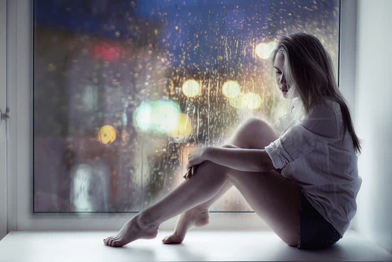 malheureuse jeune femme blonde par la fenêtre pendant qu'il pleut