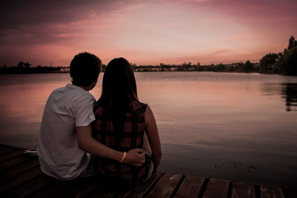 un homme et une femme s'embrassent assis à côté de la jetée