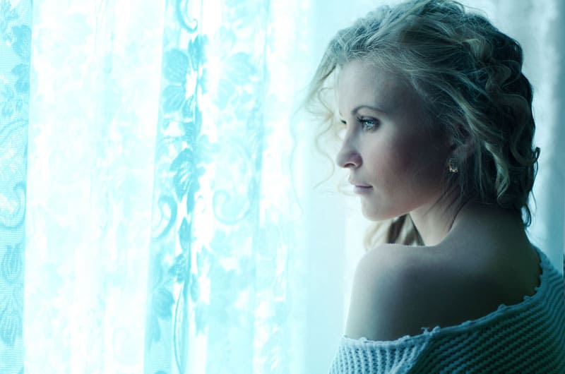 triste jeune femme blonde regardant par la fenêtre