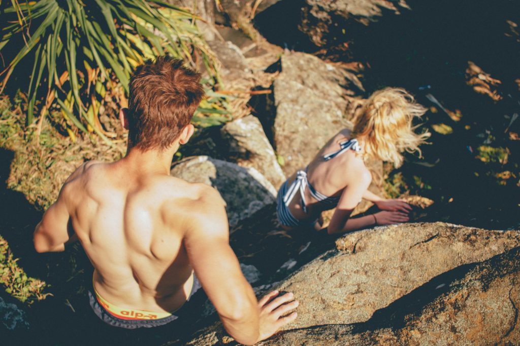 un homme et une femme descendent les rochers en maillot de bain