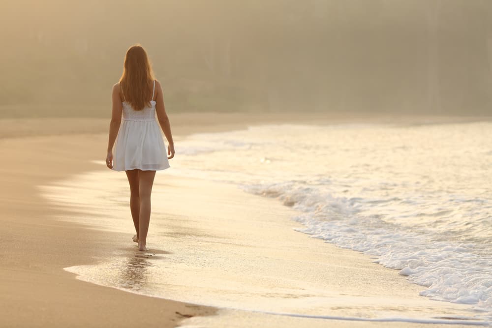 une femme en robe blanche se promène sur la plage