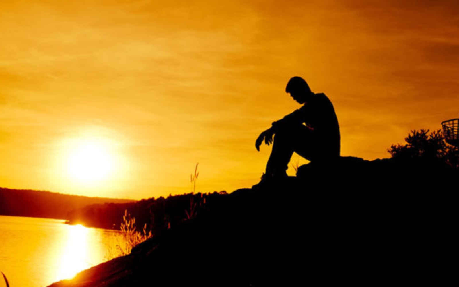 homme triste assis au bord de leau au coucher du soleil