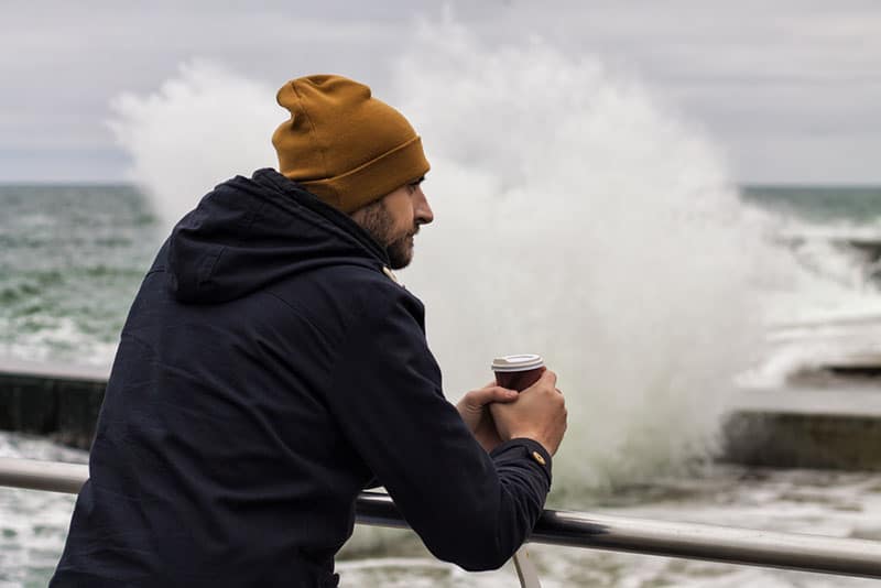 homme triste avec du café à la main au bord de l'eau
