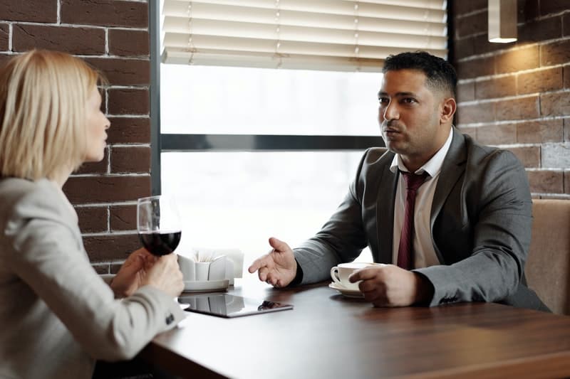un homme et une femme assis à une table, boire du vin et parler