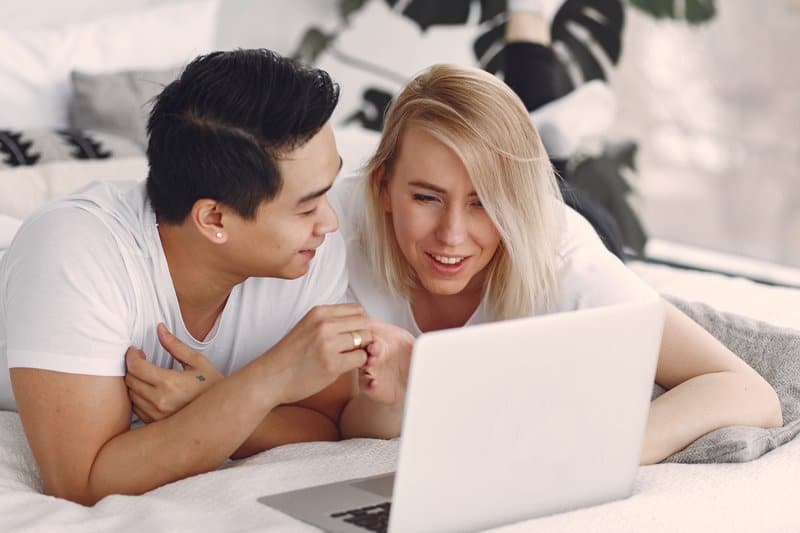un homme et une femme au lit derrière un ordinateur portable