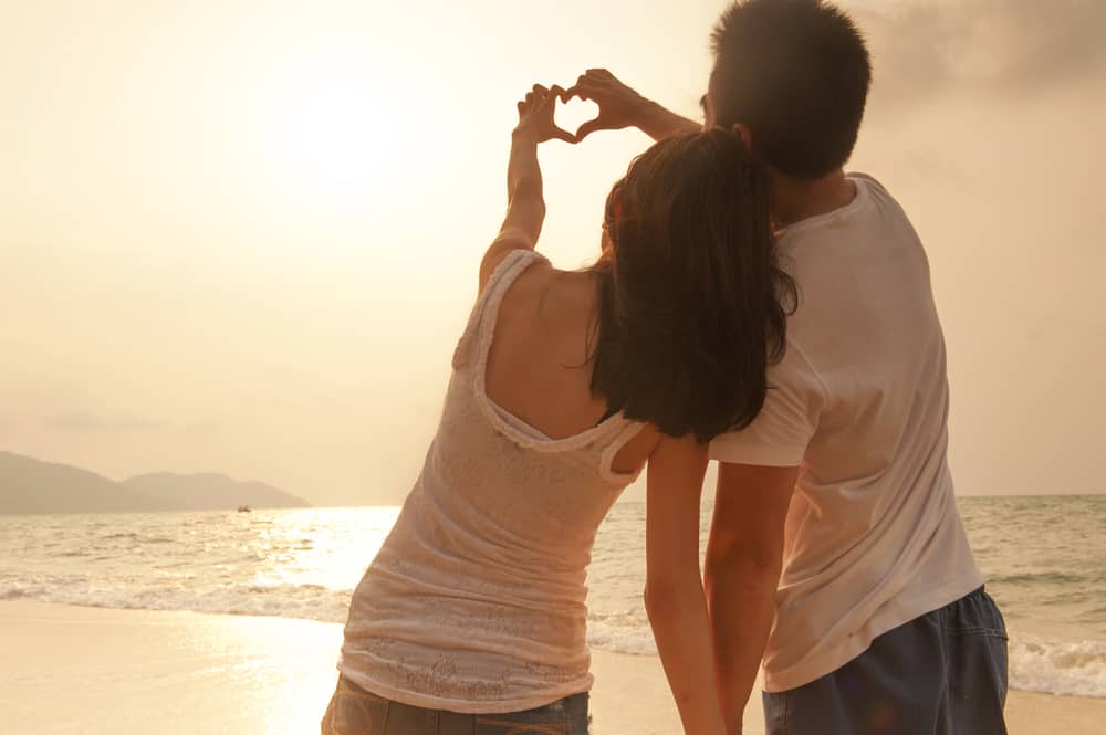 un homme et une femme sur la plage font un coeur