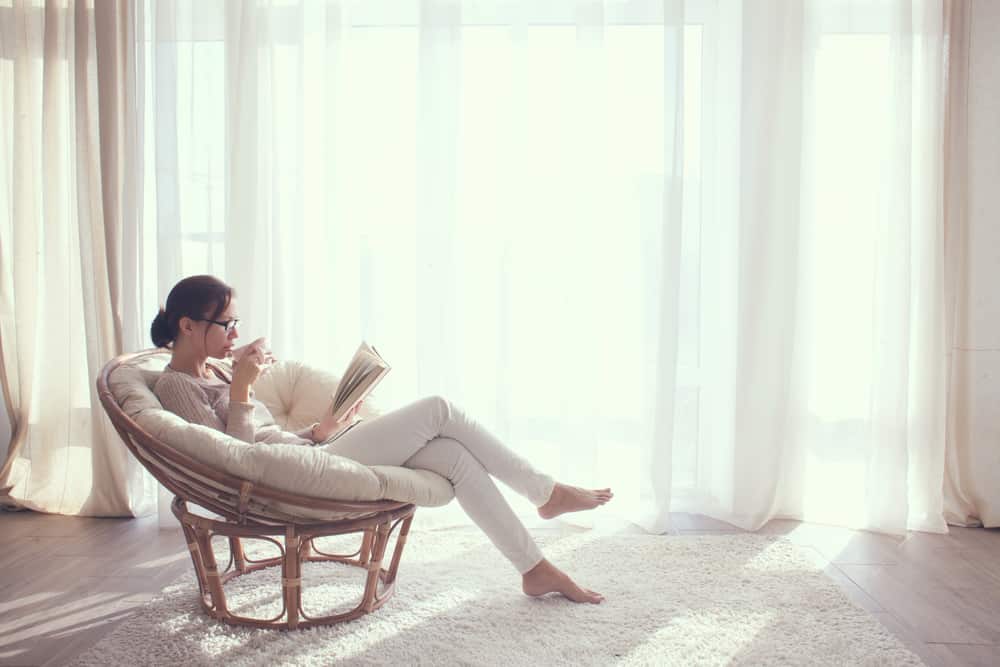 une femme assise dans un fauteuil, boire du café et lire un livre
