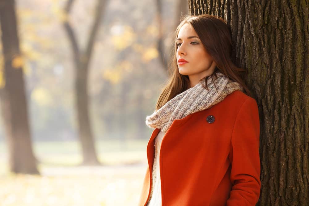 une femme avec un manteau rouge se tient appuyé contre un arbre