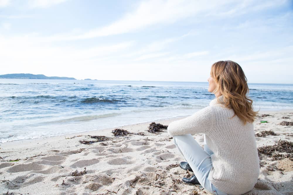 une femme est assise sur la plage et donne sur la mer