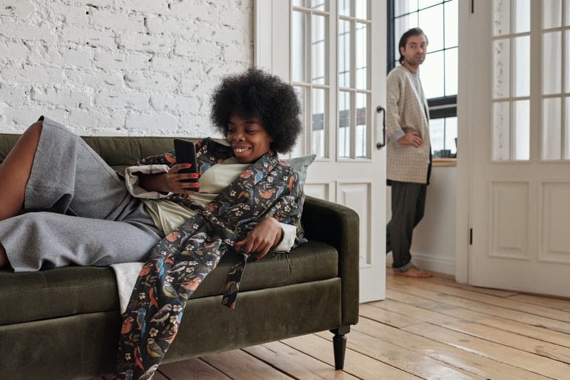 Femme sur le bouton du canapé sur le téléphone pendant qu'un homme regarde par la fenêtre