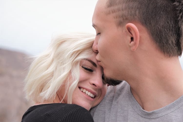 un homme embrasse une femme blonde sur le front