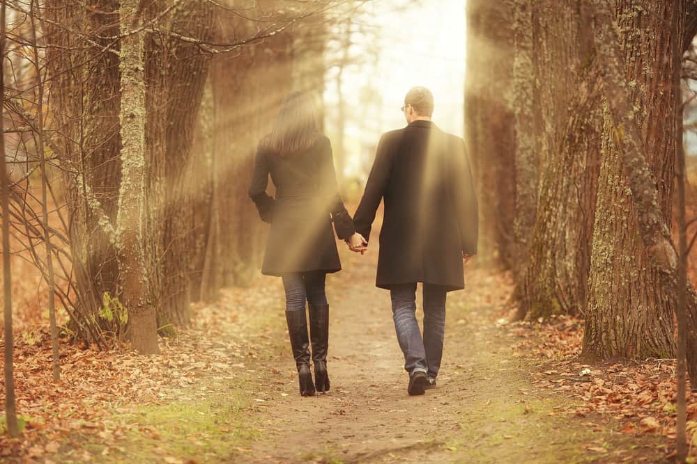 un homme et une femme marchent dans les bois en se tenant la main