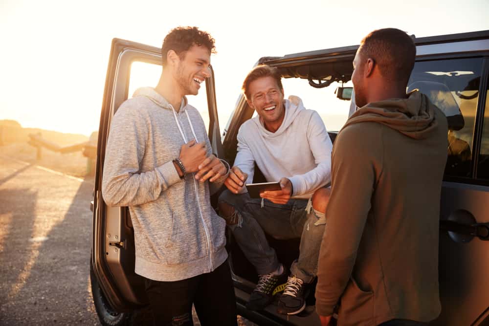 un homme se tient avec des amis à côté d'une voiture et rit