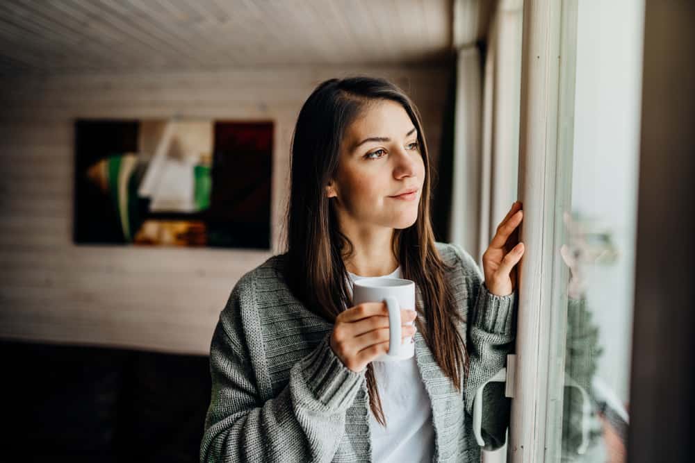 la femme boit du café et regarde par la fenêtre