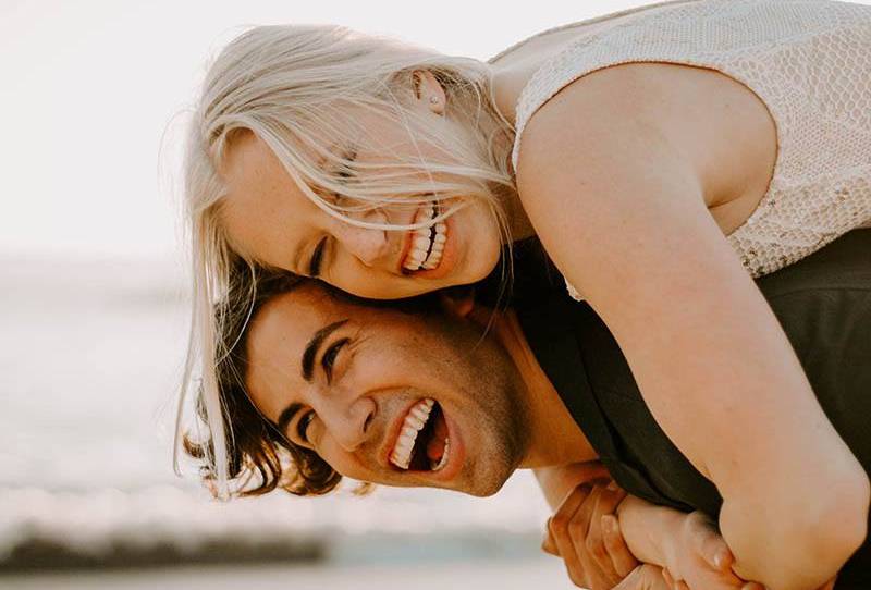 gros plan sur la photo d'un homme souriant portant une femme blonde heureuse à l'extérieur