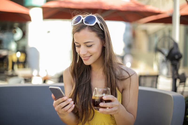 une femme boit du jus et regarde son téléphone portable