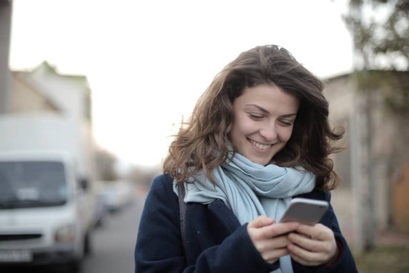 une femme joyeuse dans la rue regarde le téléphone