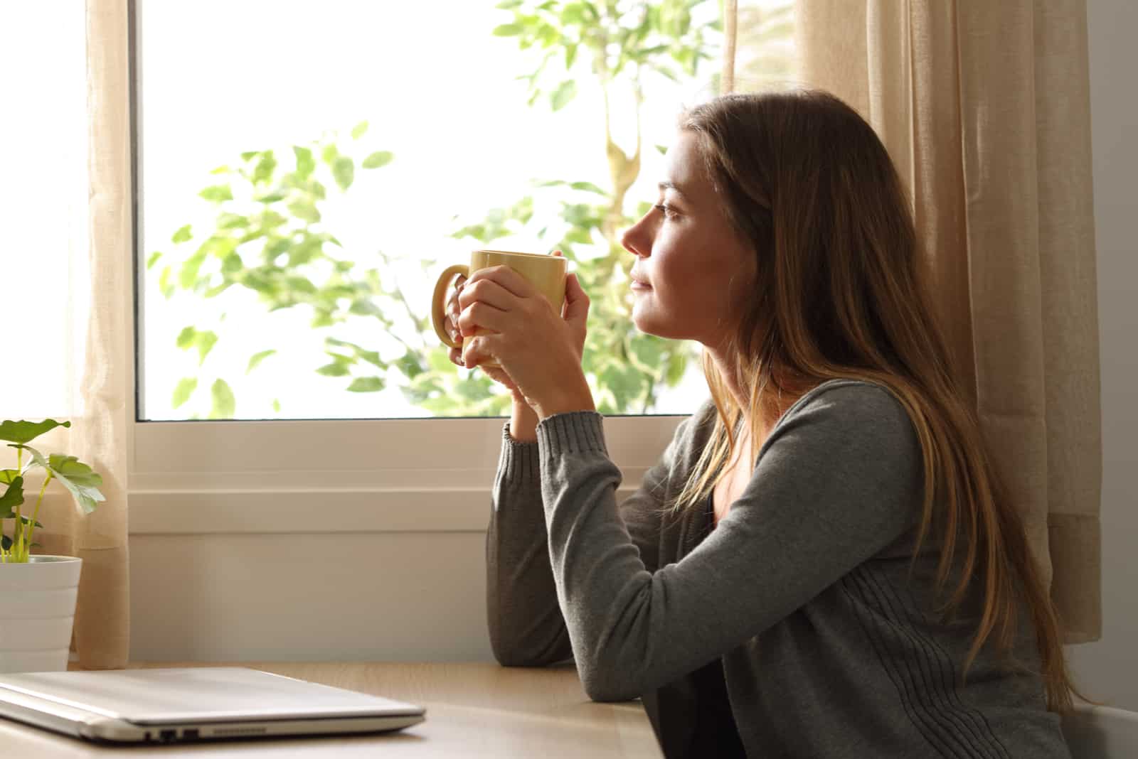 une femme aux longs cheveux bruns est assise et boit du café