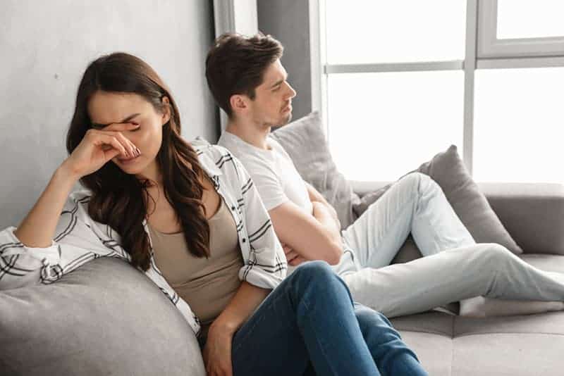Photo de couple déçu assis ensemble sur un canapé à la maison avec un regard bouleversé et exprimant une querelle isolé sur fond blanc
