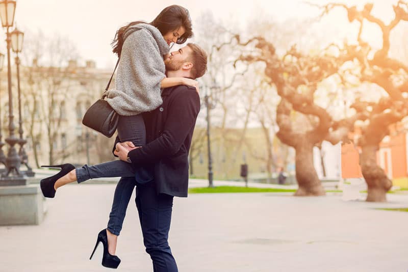 jeune homme soulevant sa belle petite amie au-dessus de lui dans le parc