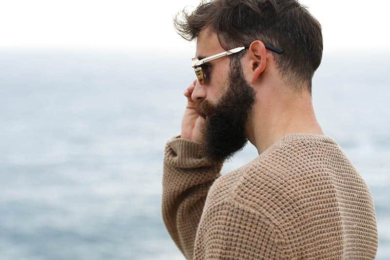Vue latérale d'un homme barbu portant des lunettes de soleil et un sweat-shirt marron à l'extérieur
