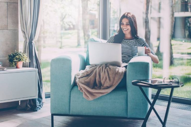 Femme s’asseyant sur l’ordinateur portatif de saisie de sofa et souriant