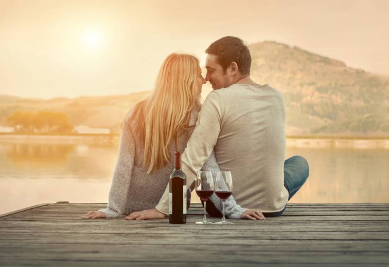 Couple romantique assis sur la jetée avec du vin rouge.