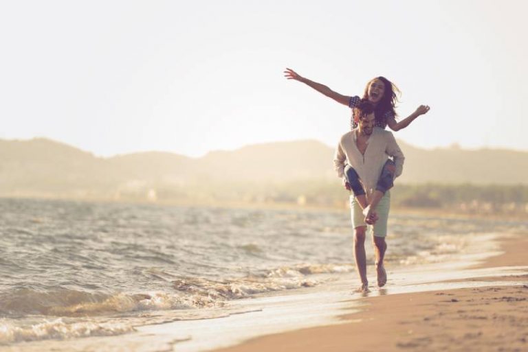 couples heureux piggybacking sur la plage