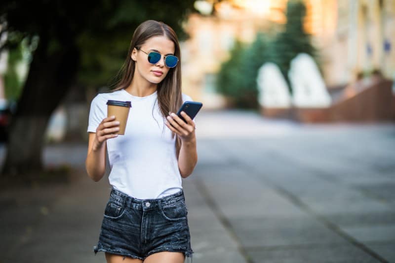 Jeune femme avec un café et un téléphone marchant dans la rue