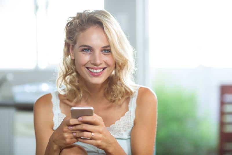 Portrait d'une femme heureuse et souriante tenant son téléphone portable à la maison