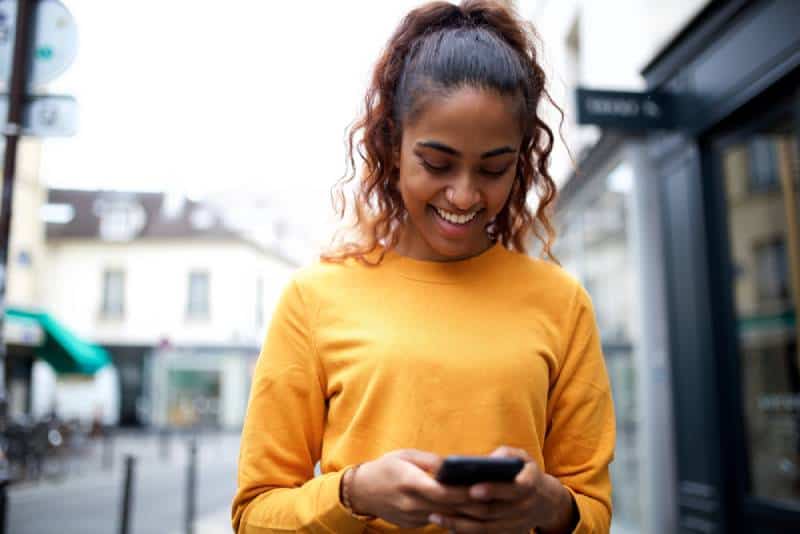 Portrait d'une jeune femme indienne heureuse regardant son téléphone portable en ville