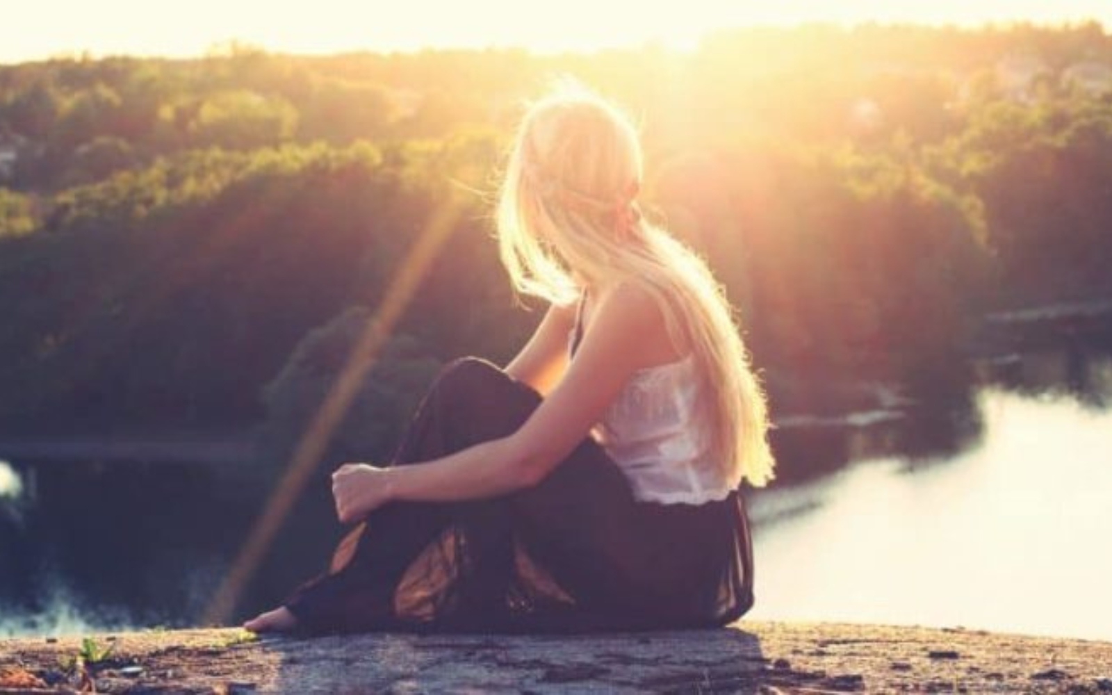 une femme blonde assise sur un rocher