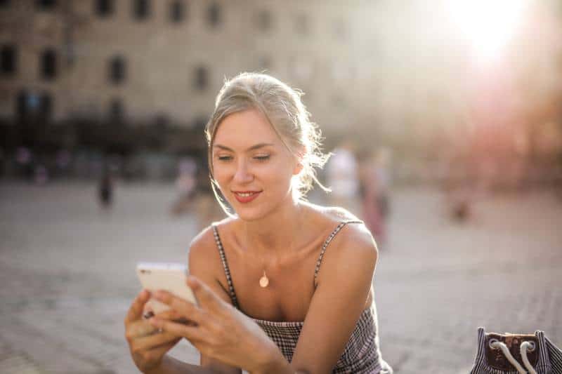 Une fille souriante envoie un SMS au téléphone à l'extérieur